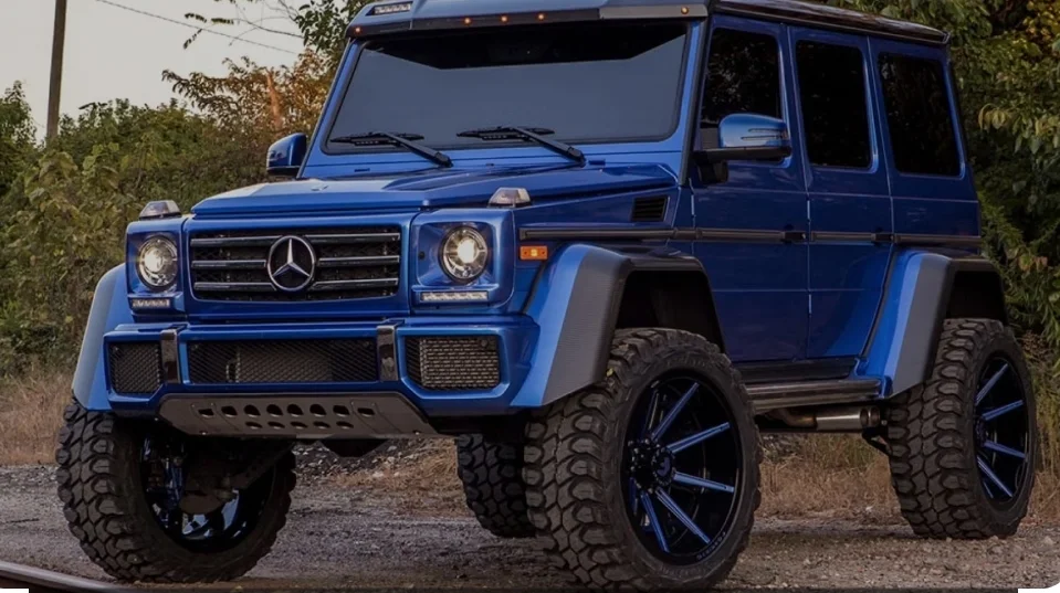 A clean blue Mercedes-Benz G-Class SUV on off-road tires, parked on a gravel road